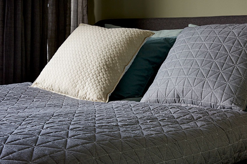 Uzglavlje kreveta sa jastucima i sivi prekrivač preko kreveta