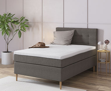 Veliki bračni boxspring krevet sive boje i pored njega moderni noćni ormarić od svijetlog drva