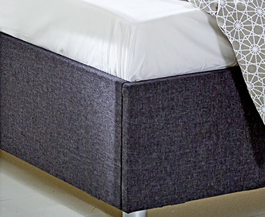 Bijela ravna plahta utrpana u ugao tapaciranog okvira kreveta sive boje
