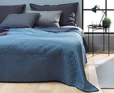 Plavi prekrivač preko velikog bračnog kreveta u spavaćoj sobi plavih tonova
