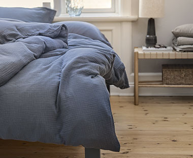 Krevet s elegantnm tamno plavom posteljinom i klupa pored njega