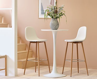 Bijele šankerske stolice skandinavskog dizajna i visoki bijeli barski stol pored nježno rozog zida